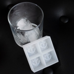 Puede incluir: Una bandeja de cubitos de hielo de silicona blanca con cuatro moldes en forma de ancla. La bandeja está llena de agua y lista para congelar.
