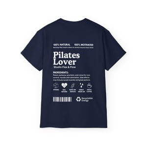 Puede incluir: Camiseta azul marino con texto blanco "Pilates Lover" y "Studio Flex & Flow". La camiseta tambi&eacute;n enumera "Ingredientes" e iconos. La camiseta est&aacute; hecha de un material suave.