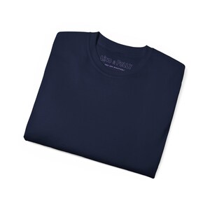 Puede incluir: Una camiseta azul marino doblada. La camiseta tiene cuello redondo y el texto "LINO & POLLY YOU ARE BEAUTIFUL" est&aacute; impreso en el cuello.