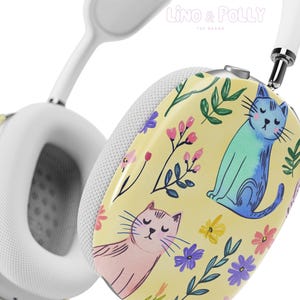 Könnte beinhalten: Weiße kabellose Kopfhörer mit einem gelben Blumen- und Katzendesign. Das Design zeigt zwei Katzen, eine blaue und eine rosa, mit geschlossenen Augen. Der Hintergrund ist hellgelb mit grünen Blättern und rosa und violetten Blumen.