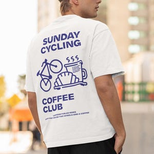Könnte beinhalten: Weißes T-Shirt mit blauem Text, der "Sunday Cycling" und "Coffee Club" lautet. Das Design beinhaltet ein Fahrrad, eine Kaffeetasse und den Text "SSS Cycling Coffee Cycling Repeat".