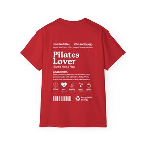 Puede incluir: Una camiseta roja con texto blanco. El texto dice "Pilates Lover" y "Studio Flex & Flow". La camiseta tambi&eacute;n enumera "Ingredientes" e iconos que representan elementos clave de Pilates. La camiseta est&aacute; hecha de material 100% natural y est&aacute; 100% motivada.