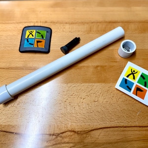 May include: A collection of items including a white tube, a black cylinder, a white cylinder, and two square stickers with a colorful logo. The items are arranged on a wooden surface.