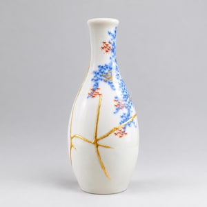 May include: A white ceramic vase featuring a slender neck and a rounded body. The surface is decorated with delicate blue and red leaf patterns, accented by prominent gold-colored lines that create a branching, crack-like design across the exterior.