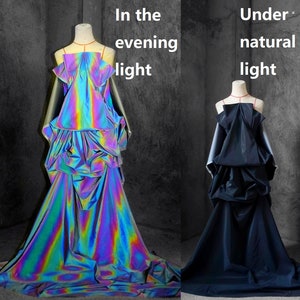 Puede incluir: Dos vestidos sobre maniquíes, uno con luz de noche y otro con luz natural. El vestido de la izquierda es iridiscente, reflejando un arcoíris de colores. El vestido de la derecha es de color azul oscuro liso. El texto de la imagen dice "In the evening light" y "Under natural light."