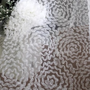 May include: White sheer fabric with a delicate, swirling floral pattern. The fabric is soft and lightweight, making it ideal for crafting and sewing projects.