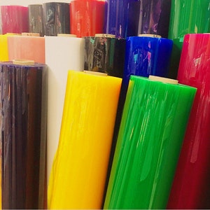 Może przedstawiać: Rolki przezroczystej folii plastikowej w różnych kolorach, w tym czerwonym, niebieskim, zielonym, żółtym i czarnym. Rolki są ułożone jedna na drugiej.