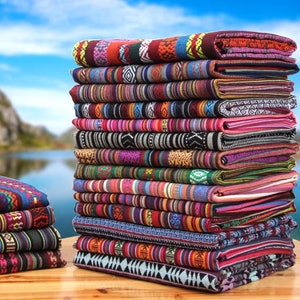 Puede incluir: Una pila de tela colorida con varios patrones y rayas. La tela está tejida con diferentes colores, incluyendo rojo, azul, verde, amarillo y negro. La tela está doblada y apilada sobre una superficie de madera.