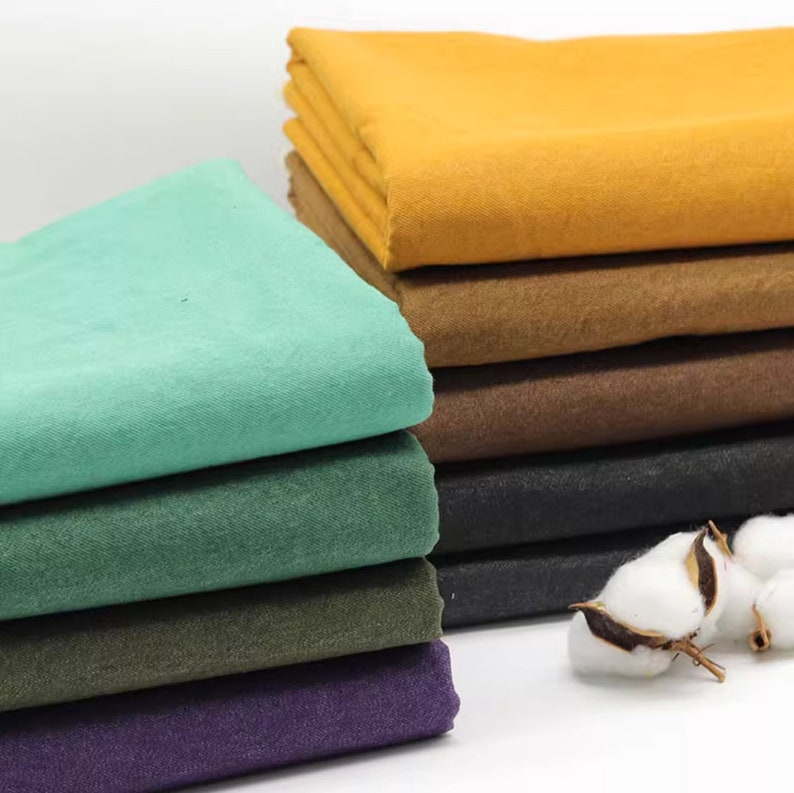 May include: Stack of fabric swatches in various colours, including green, purple, brown, and yellow. The fabric is folded and arranged in a neat pile.