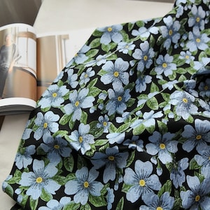 May include: Black fabric with a blue and green floral pattern. The fabric is soft and has a subtle sheen.