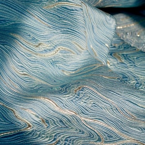 May include: Close-up of a blue fabric with a wavy, marbled pattern in silver thread. The fabric has a textured, woven look.