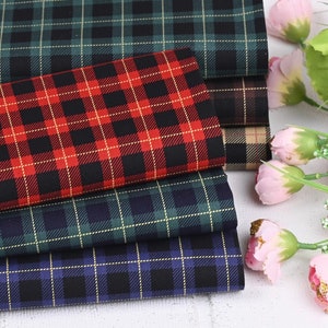 Può includere: Quattro tessuti a quadri diversi in verde, rosso, blu e marrone con accenti dorati. I tessuti sono impilati uno sopra l'altro.