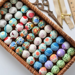 Może przedstawiać: Wickerowy kosz wypełniony kolorowymi guzikami pokrytymi tkaniną. Guziki mają różne wzory, w tym kwiatowe, geometryczne i zwierzęce.