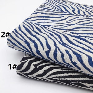 Puede incluir: Dos muestras de tela con un patrón de estampado de cebra. La muestra superior es blanca con rayas azules y está etiquetada como "2#." La muestra inferior es blanca con rayas negras y está etiquetada como "1#."