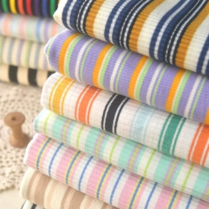 May include: A stack of striped fabric in various colors, including orange, blue, green, pink, and beige. The fabric is folded neatly and has a ribbed texture.