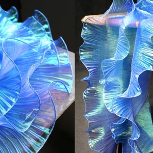 May include: Blue iridescent ruffled trim with a shimmery finish. The trim is made of a sheer fabric and has a delicate, flowing texture.
