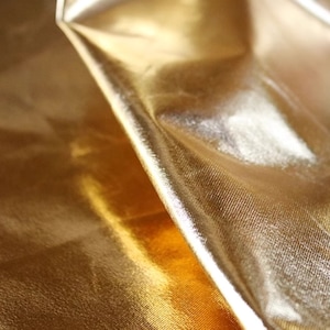 May include: Close-up of a gold fabric with a smooth, shiny texture. The fabric is folded and draped, creating a soft, flowing look.
