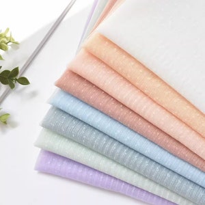 May include: A stack of seven sheer fabrics in various pastel colors, each with a subtle polka dot pattern. The fabrics are arranged in a gradient from white to lavender.