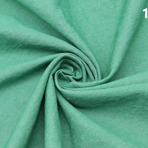May include: A close-up of a soft, green fabric with a textured surface. The fabric is folded and draped, creating a smooth, flowing look.