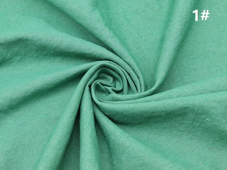May include: A close-up of a soft, green fabric with a textured surface. The fabric is folded and draped, creating a smooth, flowing look.