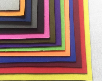 May include: A stack of 12 different colored fabric swatches. The swatches are arranged in a fan shape, with the lightest color at the top and the darkest color at the bottom. The colors are: gray, orange, navy blue, black, green, purple, red, blue, burgundy, orange, yellow, and white.