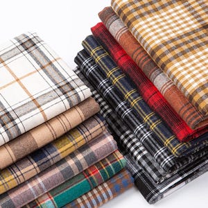 Puede incluir: Una pila de muestras de tela a cuadros en varios colores y patrones, incluyendo blanco, marrón, rojo, negro y azul.