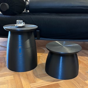 Puede incluir: Dos mesas auxiliares negras con un acabado liso y brillante. La mesa más grande tiene una tapa redonda y la mesa más pequeña tiene una tapa cuadrada. Ambas mesas están hechas de un material resistente y tienen un diseño moderno.