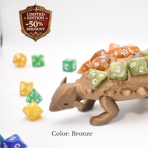 K&ouml;nnte beinhalten: Bronze-farbener W&uuml;rfelhalter in Dinosaurierform mit orangefarbenen und gr&uuml;nen W&uuml;rfeln. Der Halter ist als Ankylosaurus gestaltet. Das Bild enth&auml;lt auch ein "Limited Edition -50% Discount"-Abzeichen.