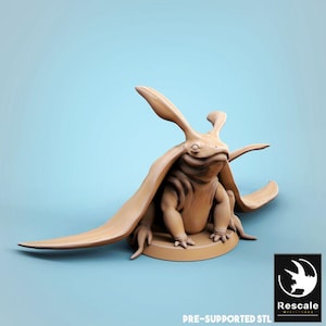Puede incluir: Figura de criatura fantástica de color marrón claro, con grandes orejas y apéndices en forma de alas. La figura está sentada sobre una base circular. El texto "PRE-SUPPORTED STL" y un logotipo son visibles.