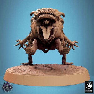 Peut inclure: Figurine de monstre marron avec une bouche ouverte, des dents pointues et une longue langue. La figurine a des mains et des pieds griffus et se tient sur une base circulaire. Les mots "Fate Unbound" et "Rescale" sont visibles.