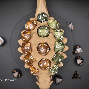 K&ouml;nnte beinhalten: Bronzefarbene W&uuml;rfel mit wei&szlig;en Zahlen, angeordnet auf einem knochenf&ouml;rmigen Halter. Die W&uuml;rfel haben verschiedene polyedrische Formen. Der Text "Color: Bronze" ist enthalten. Die W&uuml;rfel sind auf einer dunkelgrauen Oberfl&auml;che verstreut.