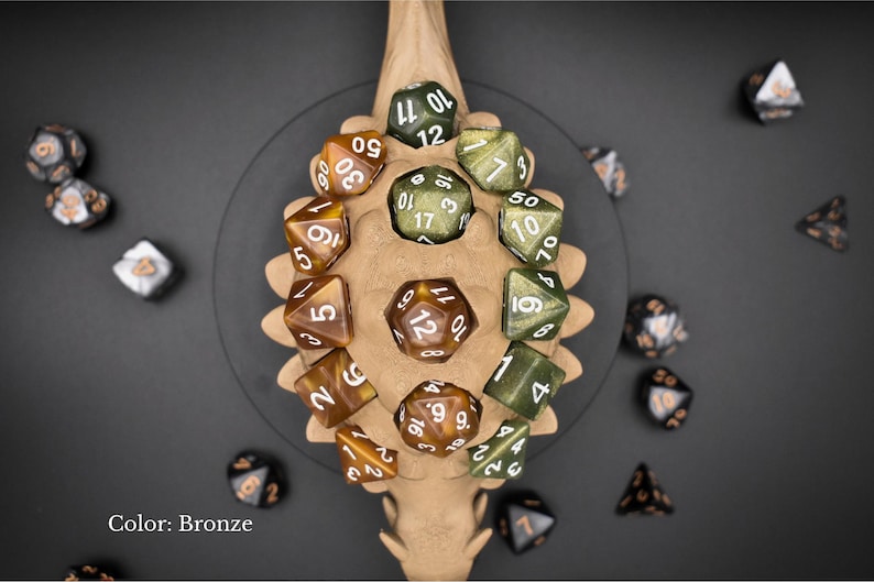 K&ouml;nnte beinhalten: Bronzefarbene W&uuml;rfel mit wei&szlig;en Zahlen, angeordnet auf einem knochenf&ouml;rmigen Halter. Die W&uuml;rfel haben verschiedene polyedrische Formen. Der Text "Color: Bronze" ist enthalten. Die W&uuml;rfel sind auf einer dunkelgrauen Oberfl&auml;che verstreut.