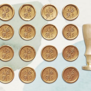 May include: A set of 16 gold wax seals with the initials "A S" and a leaf design. The seals are arranged in a grid pattern. A wooden handle for a wax seal is also included.