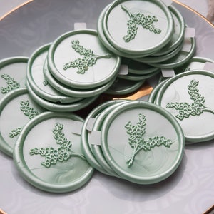 May include: A pile of sage green wax seals with a floral design. The seals are round and have a raised design.