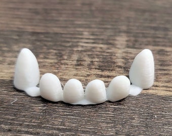 May include: A set of white dental veneers, arranged in an arch shape, resting on a wooden surface. The veneers are made of a smooth, solid material, and are designed to fit over the front teeth.