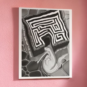 Op de afbeelding: Zwart-wit kunstafdruk van een doolhof met de tekst "YOU WERE NEVER MEANT TO BE SOLVED. TRY ALL YOU MIGHT." Het kunstwerk is ingelijst in een witte lijst en staat tegen een roze muur.