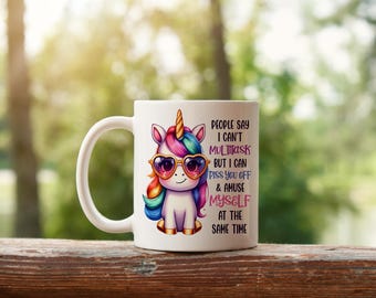 May include: White ceramic mug featuring a cartoon unicorn with rainbow hair, heart-shaped sunglasses, and gold accents. The mug has the text "PEOPLE SAY I CAN'T MULTITASK BUT I CAN PISS YOU OFF & AMUSE MYSELF AT THE SAME TIME."