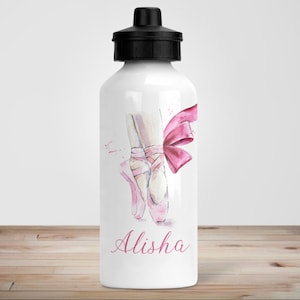 Pode incluir: Garrafa de água branca com tampa preta, com uma ilustração em aquarela de sapatilhas de ballet rosa e uma fita rosa. O nome "Alisha" está escrito em rosa. A garrafa está sobre uma superfície de madeira.