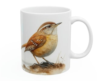 Puede incluir: Taza de cerámica blanca con una detallada ilustración a la acuarela de un chochín de Carolina. El pájaro tiene plumas marrones, beige y blancas, posado sobre un pequeño trozo de tierra. La taza tiene un asa curva.