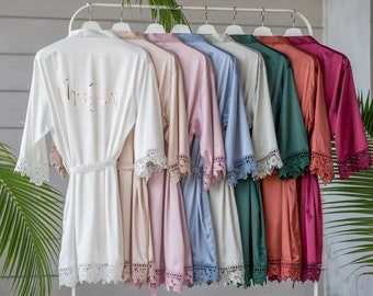 May include: A set of ten satin robes with lace trim, hanging on a rack. The robes are in various colors, including white, blush, pink, blue, beige, green, and burgundy. The white robe has the text "Mrs. Smith" embroidered on the back.