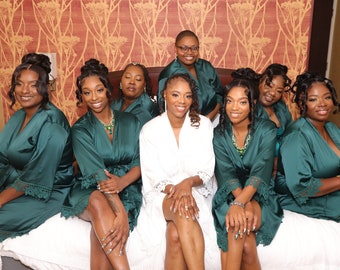 May include: A group of women wearing green satin robes with lace trim, posing for a photo. The woman in the center is wearing a white robe.