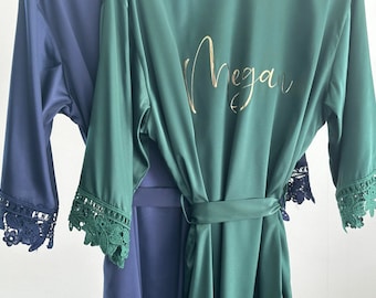 May include: A green satin robe with a gold inscription that reads "Megan". The robe has lace trim on the sleeves and a matching tie belt.