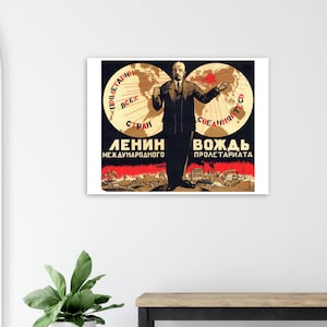 May include: A framed vintage propaganda poster featuring a black-suited man with outstretched arms, flanked by globes. The poster has red and white text in Cyrillic script, with a red band at the bottom depicting a cityscape. The background is black.