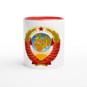 May include: White ceramic mug with a red interior. The mug features a detailed emblem with a globe, hammer and sickle, wheat stalks, and a red star. The text on the mug is in a foreign language.