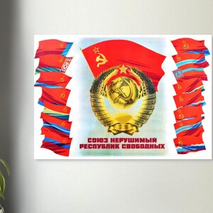May include: A framed vintage Soviet propaganda poster. The poster features a large red flag with a gold hammer and sickle emblem, surrounded by a wreath. The text "СОЮЗ НЕРУШИМЫЙ РЕСПУБЛИК СВОБОДНЫХ" is displayed in red. Several smaller flags flank the central image.