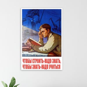 Puede incluir: Un póster vintage que muestra a un hombre leyendo un libro, con estructuras industriales de fondo. El póster tiene una combinación de colores azul y rojo, con texto en ruso. El texto dice: "Para construir, necesitas saber, para saber, necesitas aprender."
