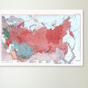May include: A framed vintage map of Russia, featuring a detailed depiction of the country's regions in shades of red, blue, and green. The map is set against a white background, with a white border, and is likely a historical or educational piece.