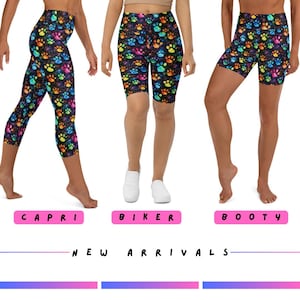 May include: Three pairs of leggings in different styles: capri, biker, and booty shorts. Each pair features a black background with a colorful paw print pattern. The text "NEW ARRIVALS" is displayed below the leggings.