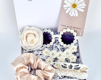 May include: A white gift box containing a pair of round white sunglasses with daisy frames, a cream-colored rose, a beige satin scrunchie, a daisy hair clip, and a gold-tone daisy bracelet. A card inside reads Flower Girl and Thank you.