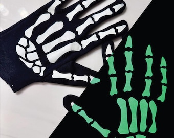 May include: A pair of black gloves with a white skeleton hand design. One glove is fully visible, while the other is partially visible with a green skeleton hand design. The gloves are likely for a Halloween costume or themed event.